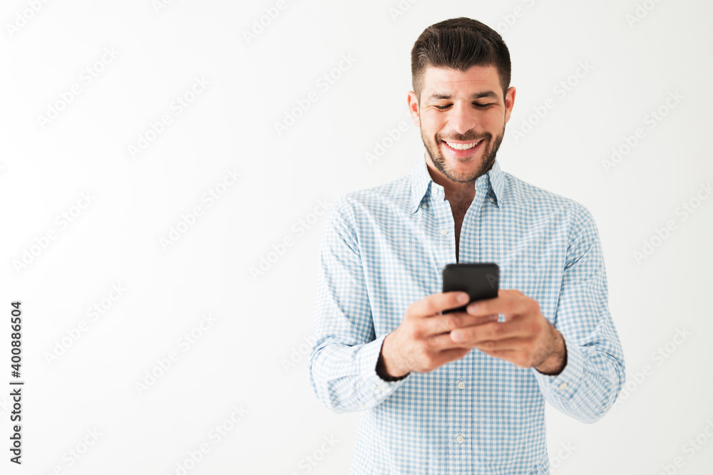 Hispanic man is happy and sending a text on his smartphone Hispanic man is happy and sending a text on his smartphone
