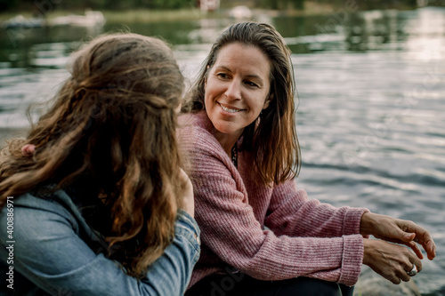Smiling mother talking to daughter while sitting by lake