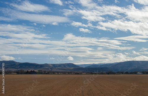 A beautiful autumn landscape on a sunny day large half is occupied by blue sky with white clouds snow-capped blue mountains trees  houses on the horizon in the distance yellow fields in the foreground