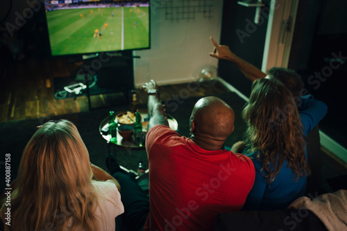 High angle view of friends watching sports on TV while sitting on sofa in living room