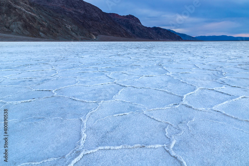 Badwater Basin at dawn  Death Valley  California. Mountains and cloudy sky in the distance. Basin floor is covered with white salt deposits  crystals form hexagonal shapes.