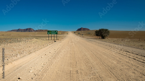 road trip in Namibia - endless straight gravel road washboard in the plains of Namib Naukluft Park - intersection of two gravel roads - green road sign Solitaire-Windhoek 