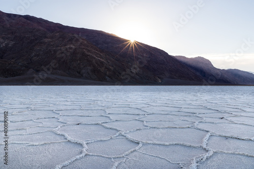 Sunrise over Badwater Basin, Death Valley, California. Sunburst over the far mountains; the basin floor is covered with white salt deposits; crystals form hexagonal shapes.
