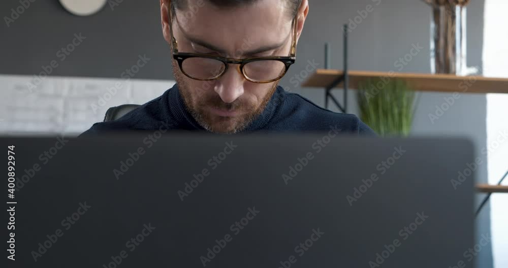 Attractive Business Man or Professor is working on Laptop in modern Office. Handsome Man working concentrated on Computer, wearing trendy Eyeglasses. Working hard. Intelligent People. Men. Attractive Business Man or Professor is working on Laptop in modern Office. Handsome Man working concentrated on Computer, wearing trendy Eyeglasses. Working hard. Intelligent People. Men.