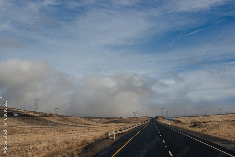 Fototapeta premium A beautiful landscape with a highway along which cars and trucks drive, on a sunny autumn day among the mountains, a blue sky with fluffy gray-blue clouds. Oregon, USA, 12-5-2019