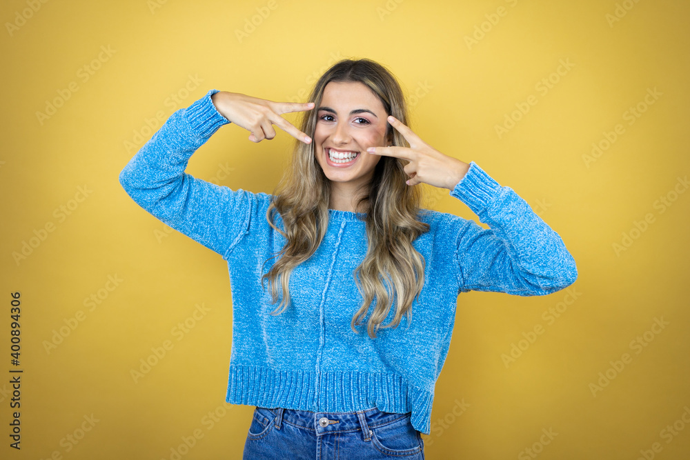 Pretty blonde woman with long hair standing over yellow background Doing peace symbol with fingers over face, smiling cheerful showing victory Pretty blonde woman with long hair standing over yellow background Doing peace symbol with fingers over face, smiling cheerful showing victory
