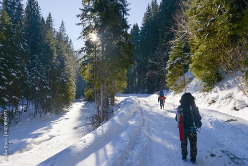 Two travelers with an backpacks walks a snowy mountain forest