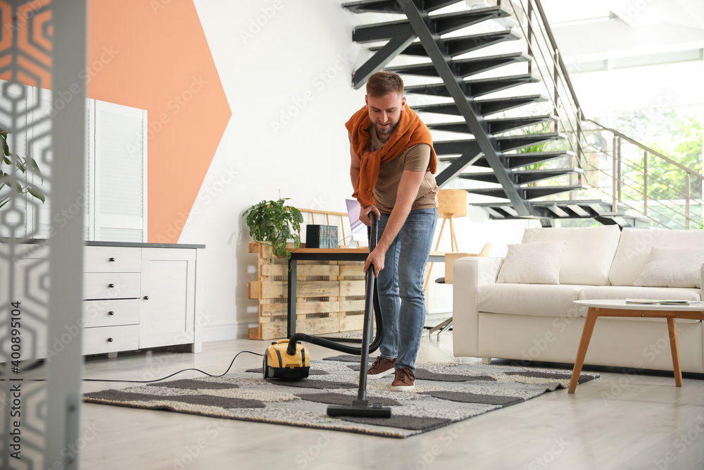 Young man using vacuum cleaner in living room