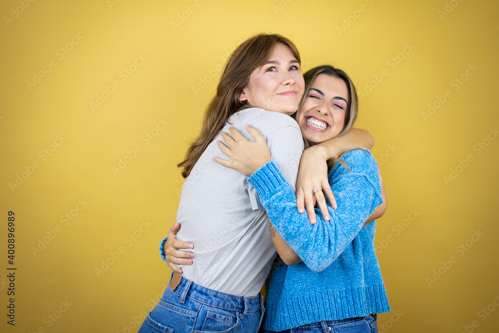 Two pretty women standing over yellow background having fun Two pretty women standing over yellow background having fun