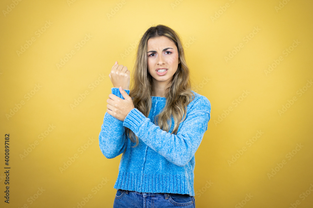 Pretty blonde woman with long hair standing over yellow background suffering pain on hands and fingers, arthritis inflammation