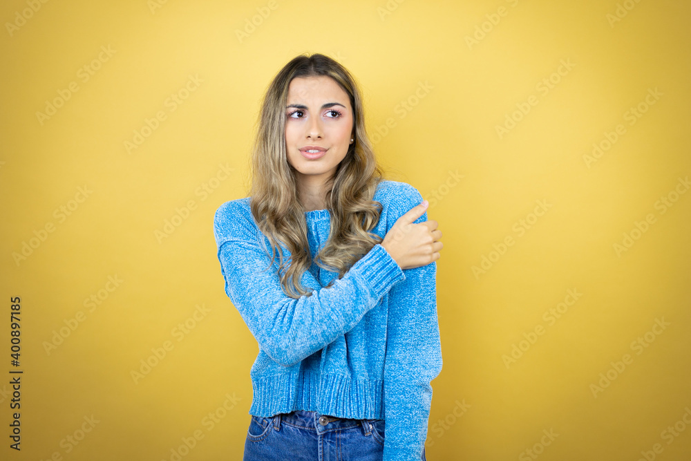 Pretty blonde woman with long hair standing over yellow background with pain on her shoulder and a painful expression Pretty blonde woman with long hair standing over yellow background with pain on her shoulder and a painful expression