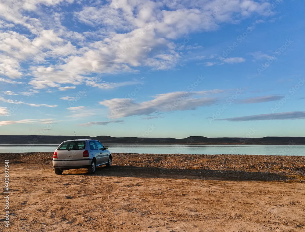 beautiful scenery and an unrecognizable gray car with no markings or information to recognize it, stunning scenery of an estuary overlooking the water, mountains, the light brown lands and the blue sk