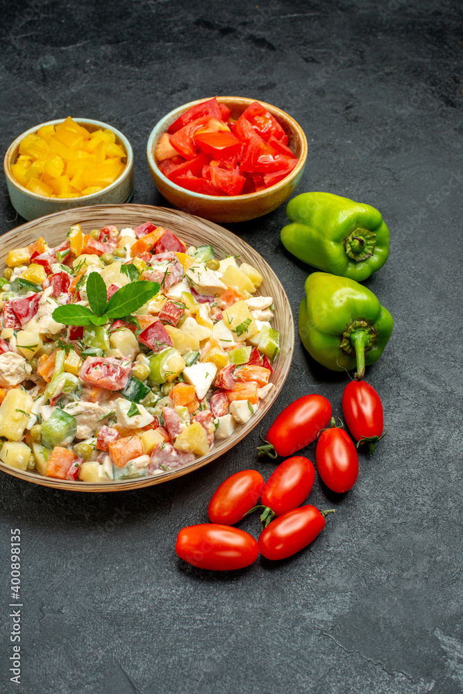 side close view of bowl of vegetable salad with different vegetables on side on dark grey background