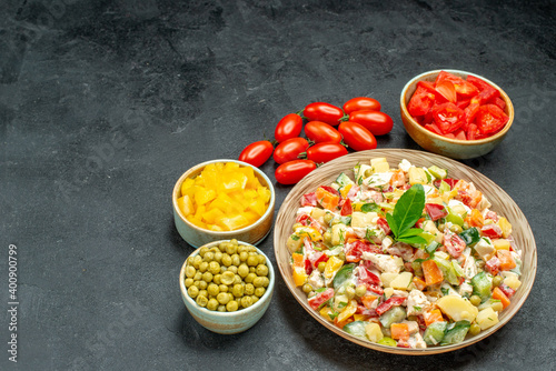 side close view of bowl of vegetable salad with vegetables on side and place for your text on dark grey background