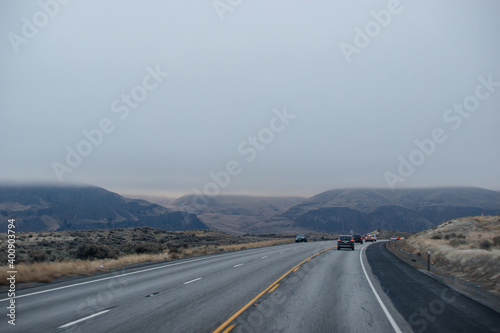 A winding asphalt road at dusk among the high blue mountains in late autumn  along which trucks and cars drive with the headlights on. Oregon  USA  02-07-2020