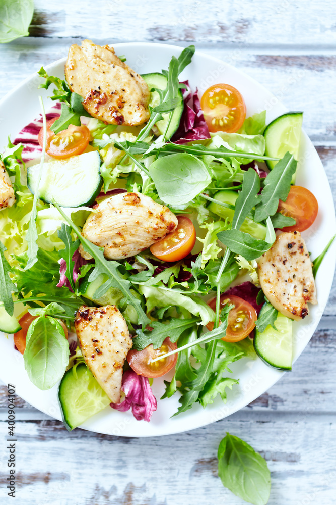Salad with Chicken Breast, Cherry Tomatoes, Cucumber, Rocket and fresh Basil. Bright wooden background. Top view. Close up. 