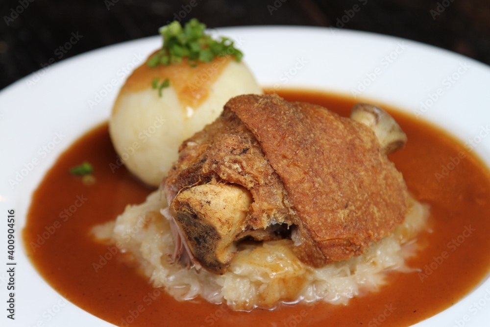 Half Bavarian pork knuckle served on sauerkraut and with potato dumpling on gravy