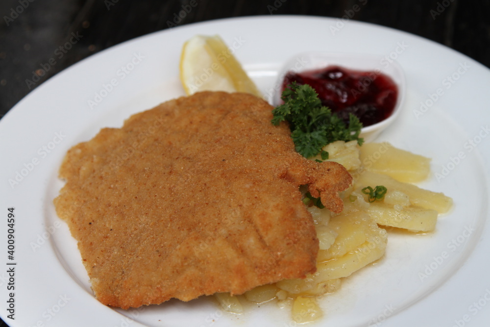 Crumbed pork escalope named Schnitzel, served with potato salad, cranberry jam and lemon Crumbed pork escalope named Schnitzel, served with potato salad, cranberry jam and lemon