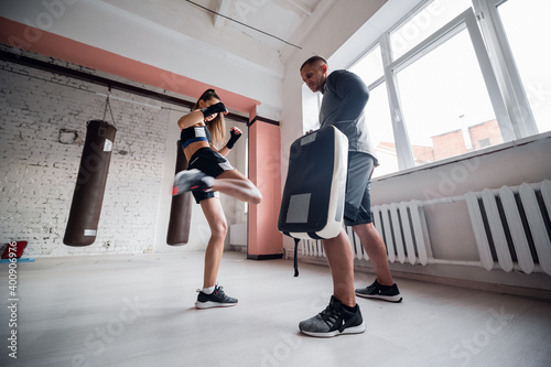 Quadro su tela A young strong kickboxer girl kicks her sparring partner with a boxing paw in a