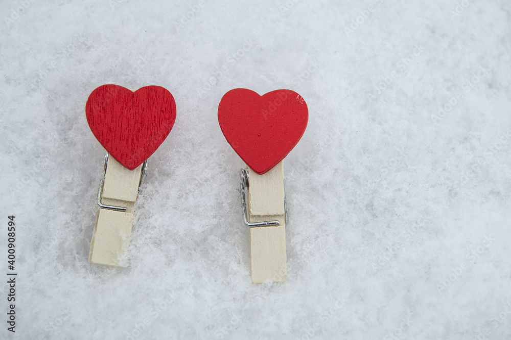 Decorative wooden clothespins in the form of two red hearts lie on the snow, the Concept of love and Valentine's Day