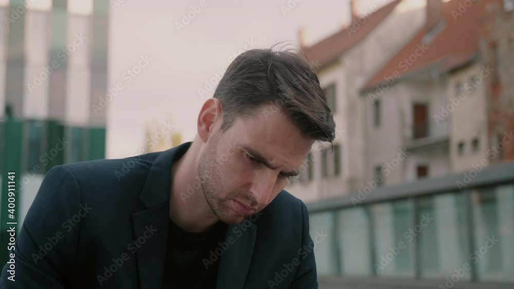 Businessman in a black suit sitting and looking down with a serious expression Businessman in a black suit sitting and looking down with a serious expression