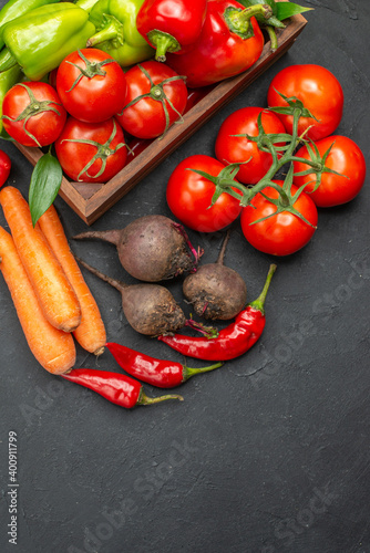Vertical view of vegetable basket with a bunch of green and peppers cucumber and tomatoes with stem carrots beets on dark background above view