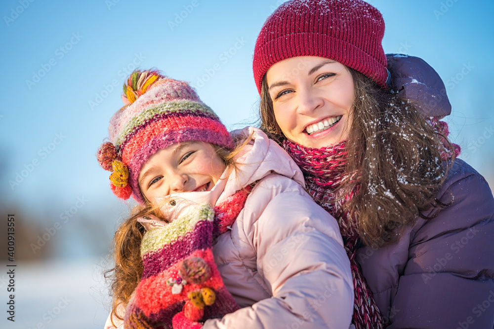 Fototapeta premium Little girl and her mother playing outdoors at sunny winter day. Active winter holydays concept.