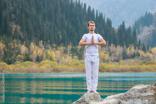 A young man in white practices yoga in the mountains. Pose Samasthiti namaskar. photo