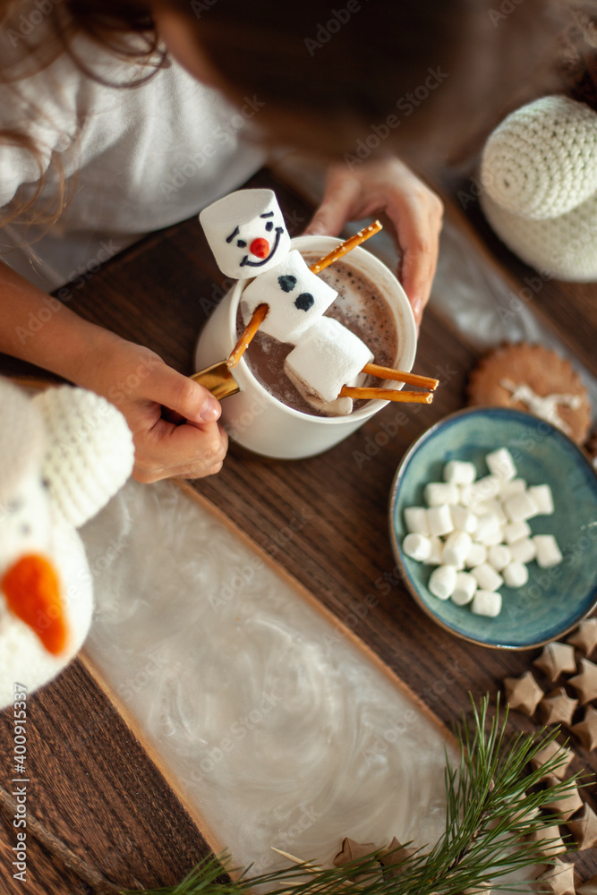 Little cute girl plays with knitted snowmen and eats gingerbread and drinks cocoa with marshmallows.