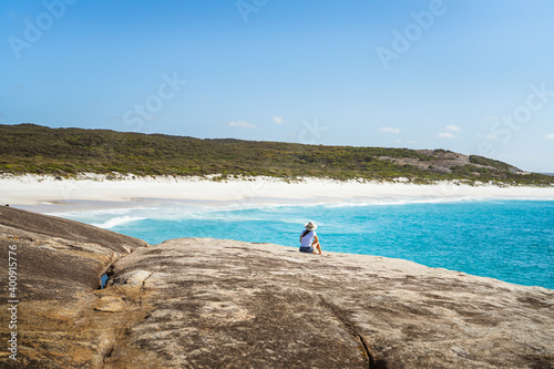 A lone woman watching the waves crash against the rocks on an empty beach. 