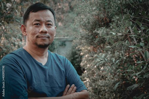 Portrait of a middle-aged man standing with his arms crossed with a proud expression in the garden.