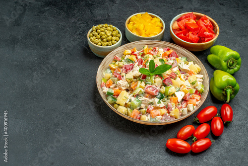 side view of bowl of vegetable salad with different vegetables on side on dark grey background
