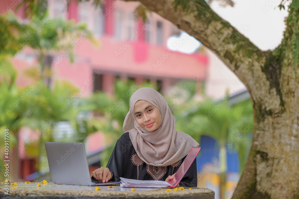 Naklejka premium Photo of beautiful islamic female studentwearing headscarf sitting in park and using silver laptop.