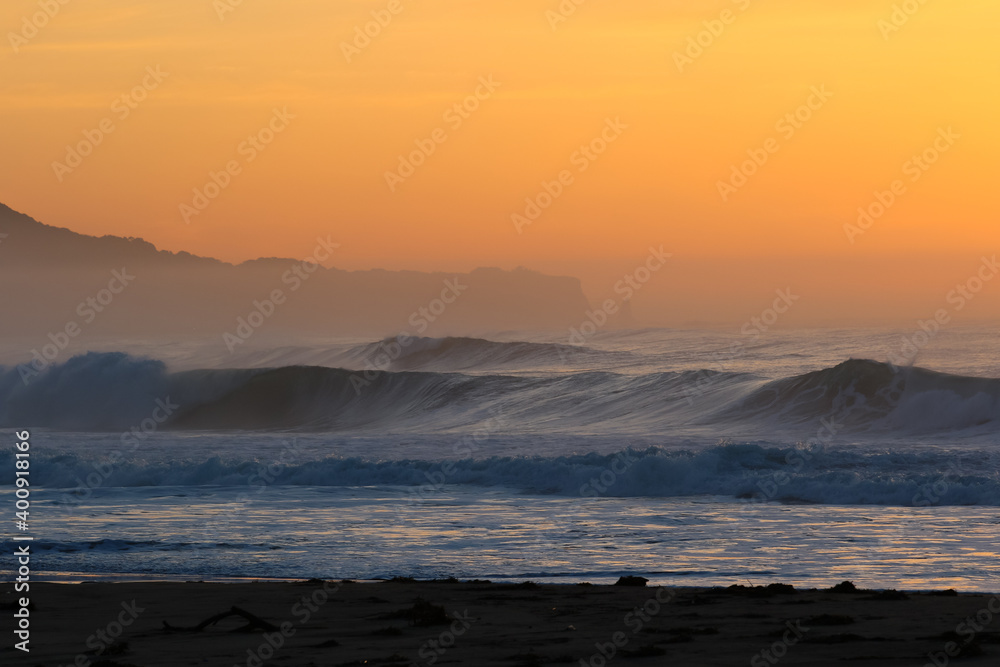 Misty Sunrise on the beach in Japan with large waves breaking onto the sand. It's a stunning scene in a place that is often referred to as the Land of the Rising Sun