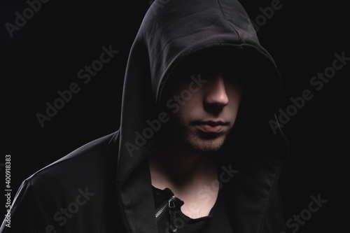 A large man in a hood and a black sweater with hands in a gesture of strength. Studio portrait with dark face anonymous thief or hacker