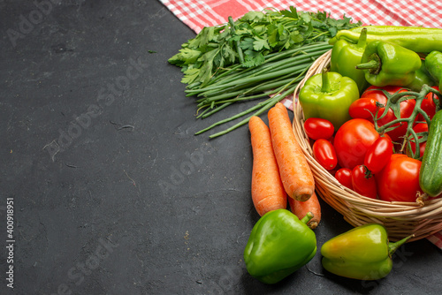 Front view of fresh various organic vegetables in a wooden basket on orange stripped towel on dark background