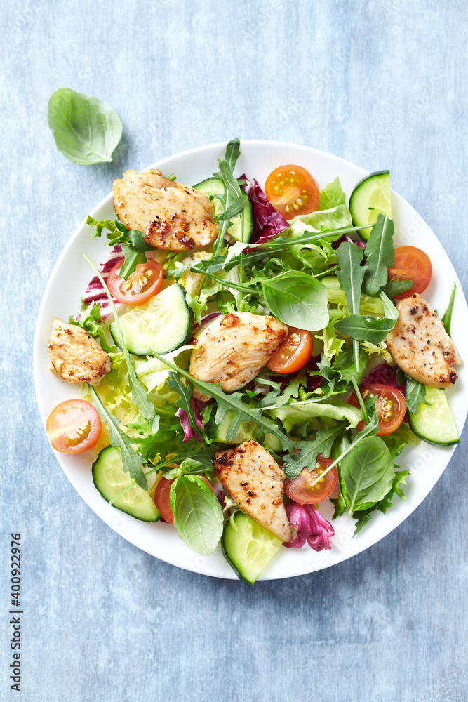 Salad with Chicken Breast, Cherry Tomatoes, Cucumber, Rocket and fresh Basil. Bright wooden background. Top view. Close up. Salad with Chicken Breast, Cherry Tomatoes, Cucumber, Rocket and fresh Basil. Bright wooden background. Top view. Close up.