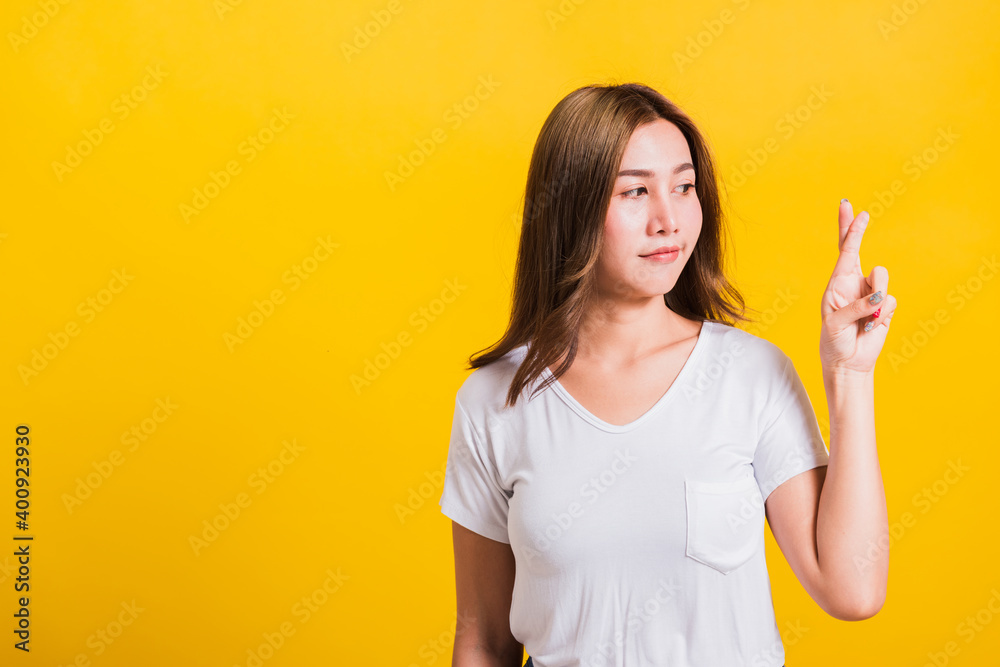 Asian Thai happy portrait beautiful cute young woman smile have superstition her holding fingers crossed for good luck and looking to camera, studio shot isolated on yellow background with copy space Asian Thai happy portrait beautiful cute young woman smile have superstition her holding fingers crossed for good luck and looking to camera, studio shot isolated on yellow background with copy space
