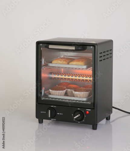 Electric small kitchen oven with bread and cup cake isolated on white