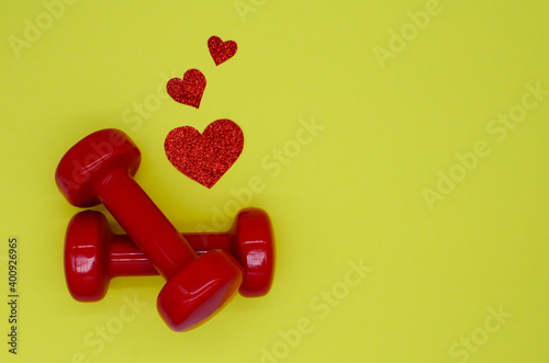 Two red dumbbells and hearts on a yellow background with copy space. Concept of Valentines day, healthy lifestyle, giving gifts, love of sports, shopping