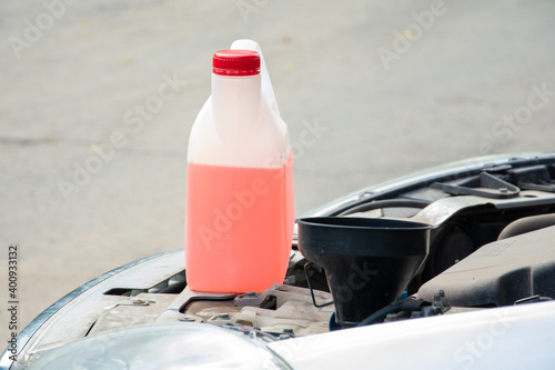 Under the open hood of the car is a white canister of pink liquid. fluid replacement.