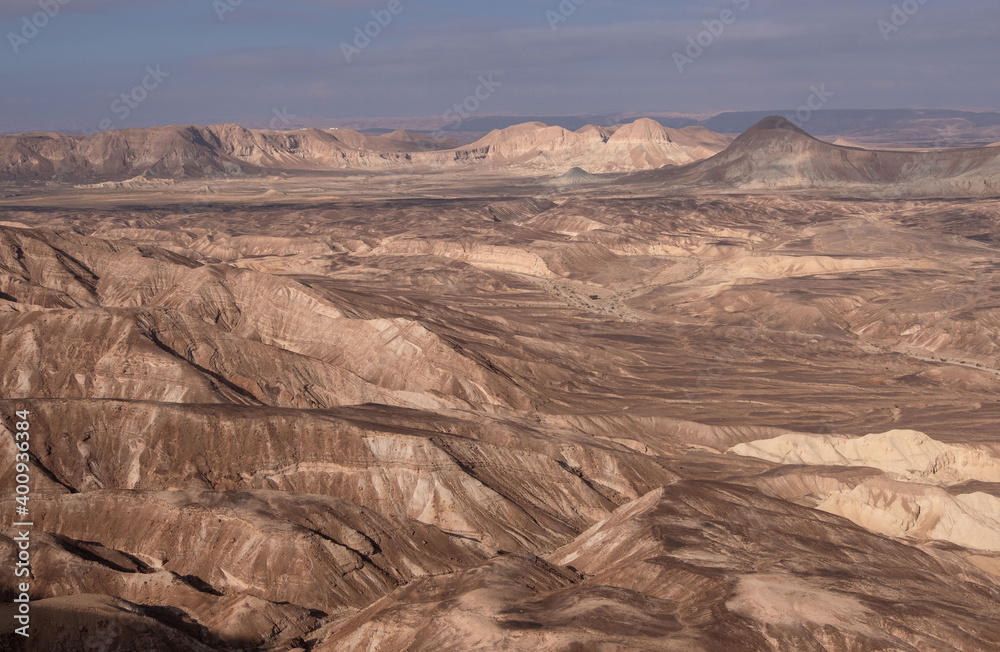 Fototapeta premium Majestic mountain range in a remote part of Negev desert, Israel. Panoramic landscape of dry wadies, colorful sandy hills, mountain folds and rock formations. The harsh beauty of the desert.