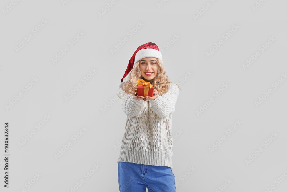 Beautiful young woman in Santa hat with gift box on light background Beautiful young woman in Santa hat with gift box on light background