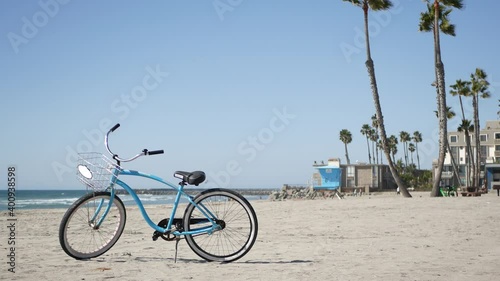 Blue bicycle, cruiser bike by sandy ocean beach, pacific coast near Oceanside pier, California USA. Summertime vacations, sea shore. Vintage cycle, tropical palm trees, lifeguard tower watchtower hut