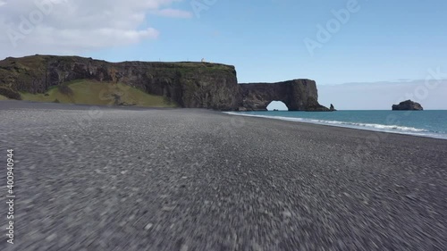 High definition drone aerial video flying along black sand beach and through rock arch formation.