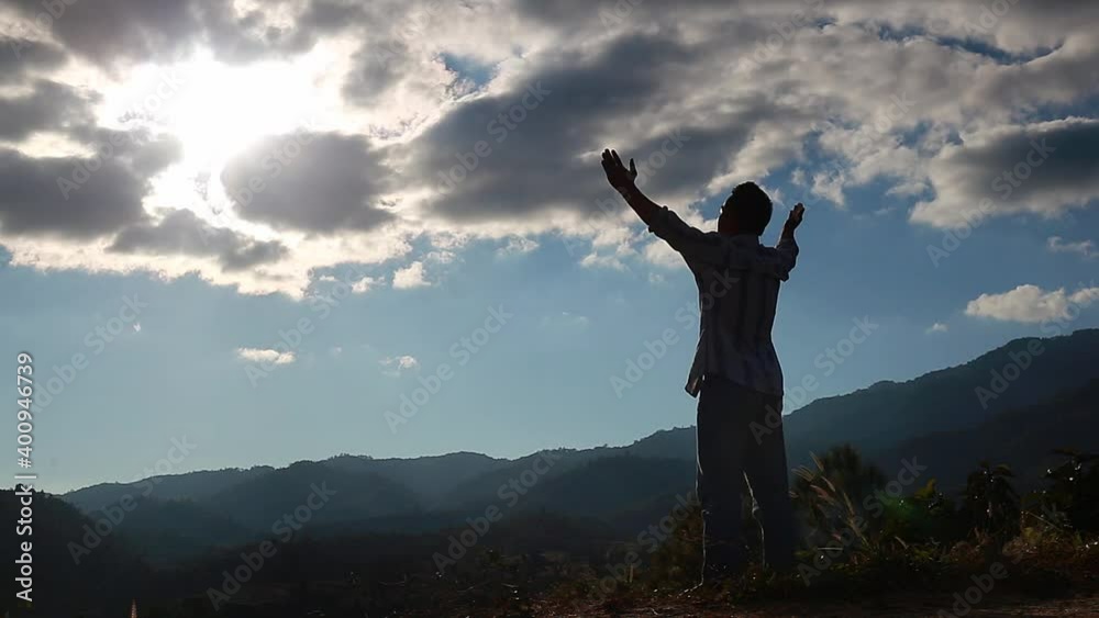 A man with hands raised standing on a mountaintop