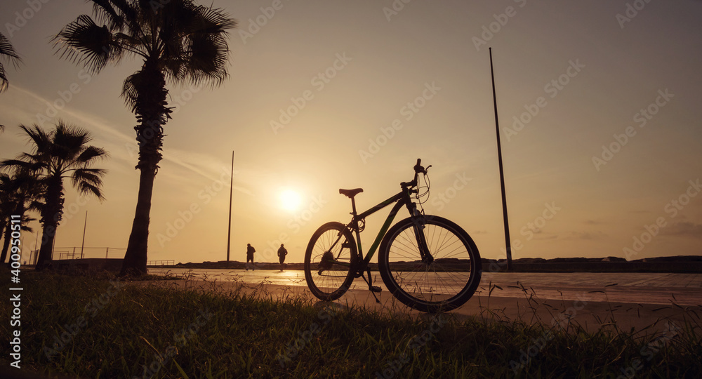 Fototapeta premium Silhouette of a bike at sunset. The sun shines through the bicycle wheel at sea side park