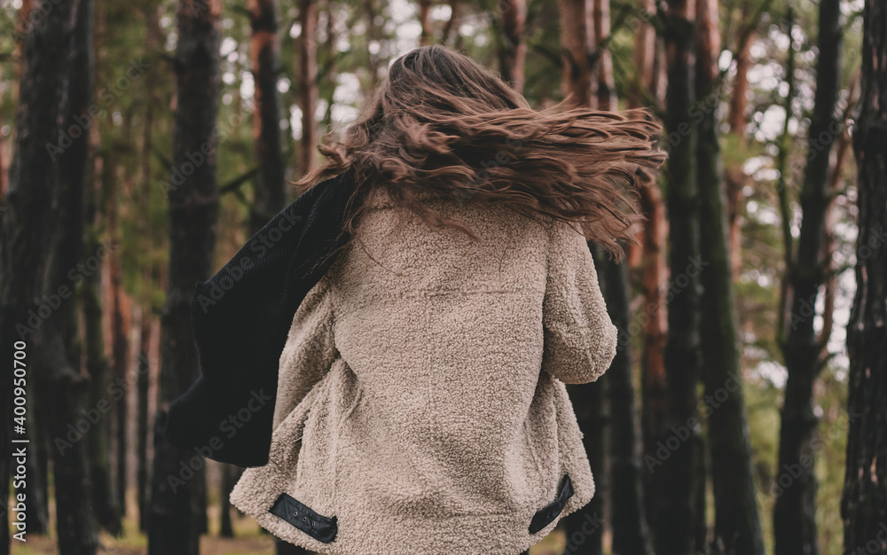 a woman of model appearance with long dark hair that flies in the wind holds a scarf in her hands and smiles while in a pine forest a woman of model appearance with long dark hair that flies in the wind holds a scarf in her hands and smiles while in a pine forest