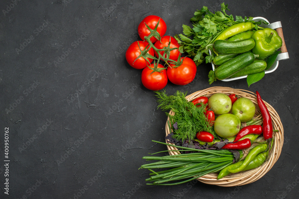 Two vegetable baskets with a bunch of green and peppers cucumber and tomatoes with stem on dark background Two vegetable baskets with a bunch of green and peppers cucumber and tomatoes with stem on dark background