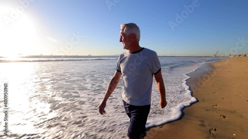 64 year old man walking at the beach near sunset. photo